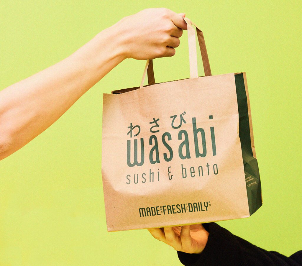 A hand is passing a brown paper bag with 