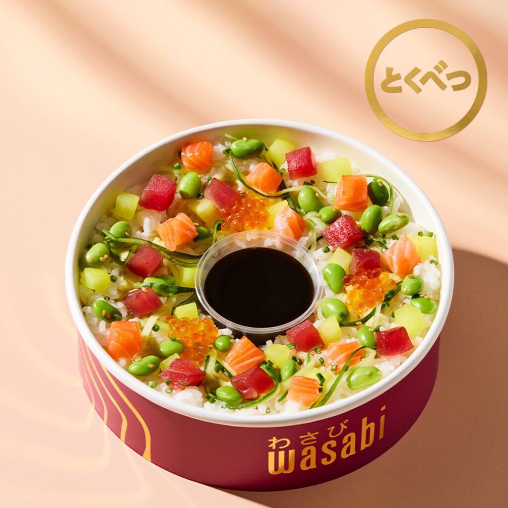 A colorful poke bowl with diced salmon, tuna, cucumber, edamame, seaweed, and fish roe on rice, arranged in a circular container with a central cup of soy sauce. The word 